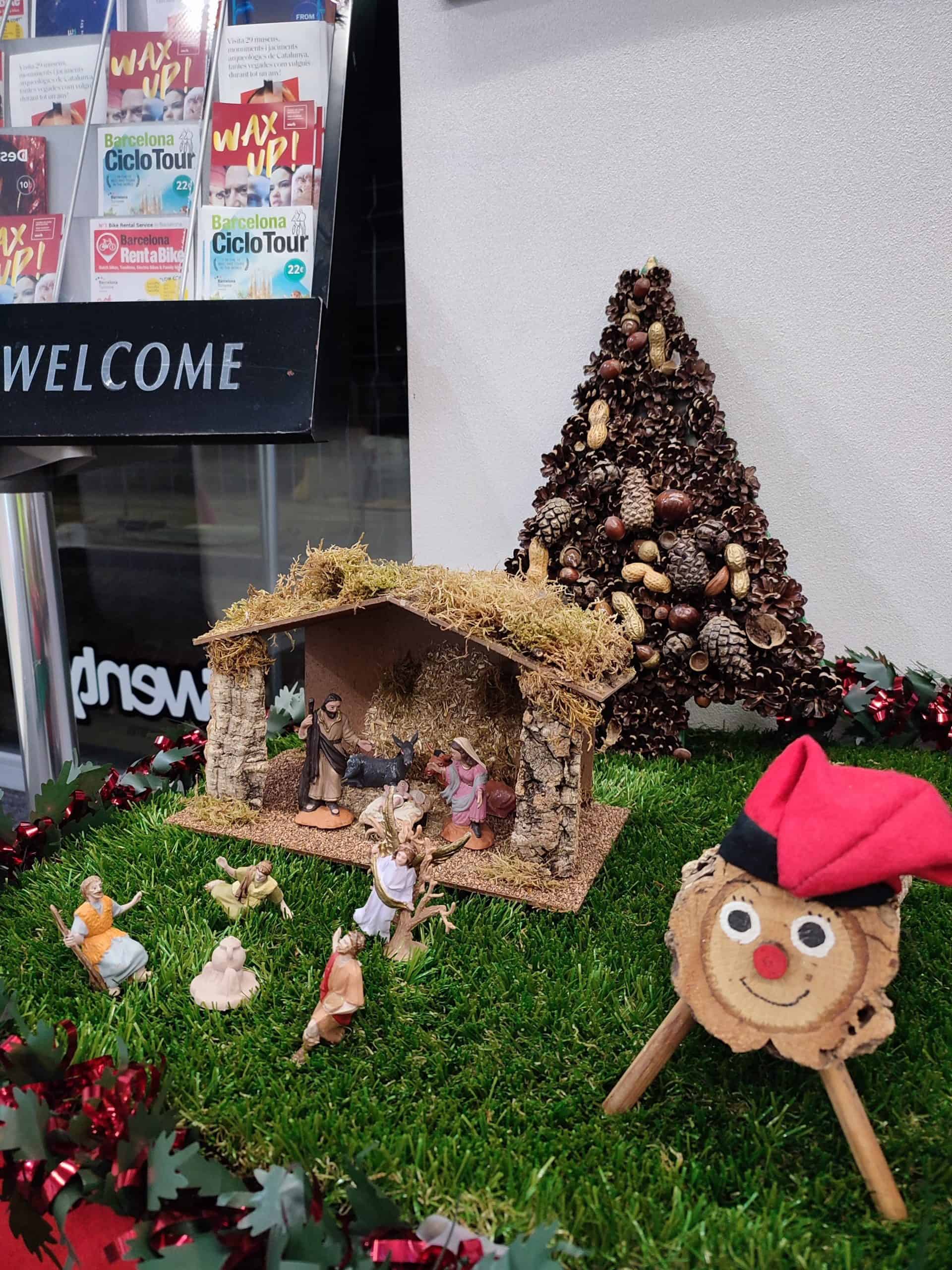 Belén navideño y un Tió de Nadal junto a un árbol decorativo natural.