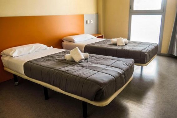 Habitación de TwentyTú Hostel con dos camas individuales, con sábanas y toallas ordenadas.