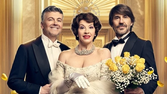 Tres personas elegantemente vestidas posan en un entorno lujoso y dorado.