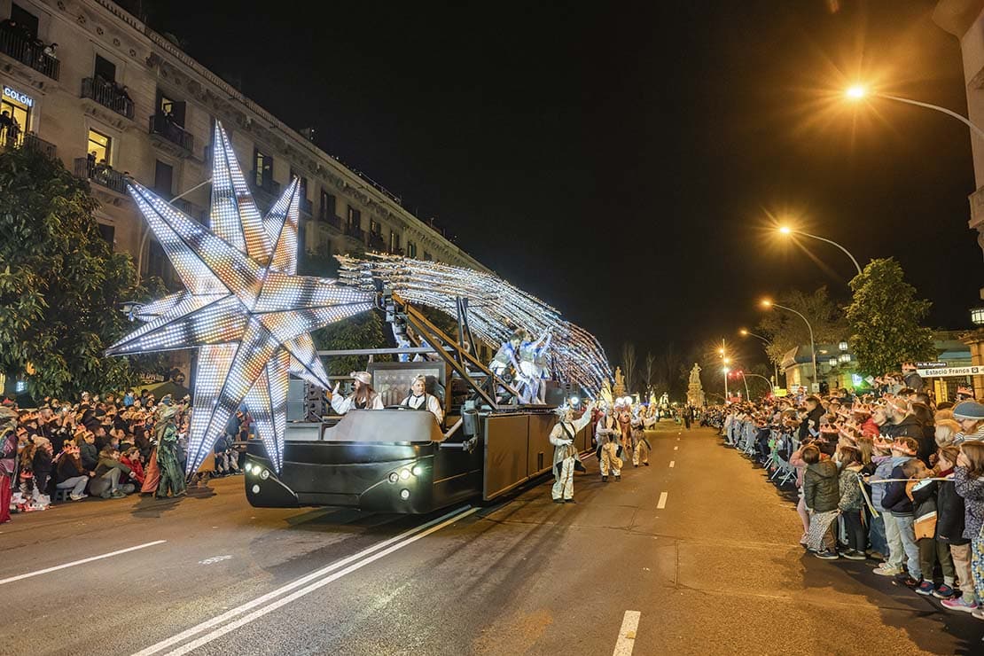 Cabalgata de Reyes Magos en Barcelona con carroza iluminada y estrella gigante recorriendo una avenida llena de público.