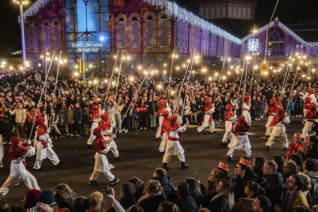 Desfile tradicional de la Cabalgata de Reyes Magos con bailarines y antorchas frente al mercado del Born en Barcelona.