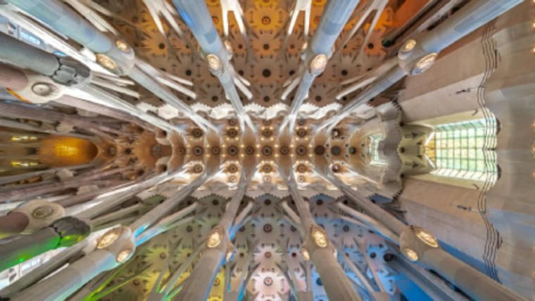Techo interior de la Sagrada Familia con columnas y vitrales de colores.