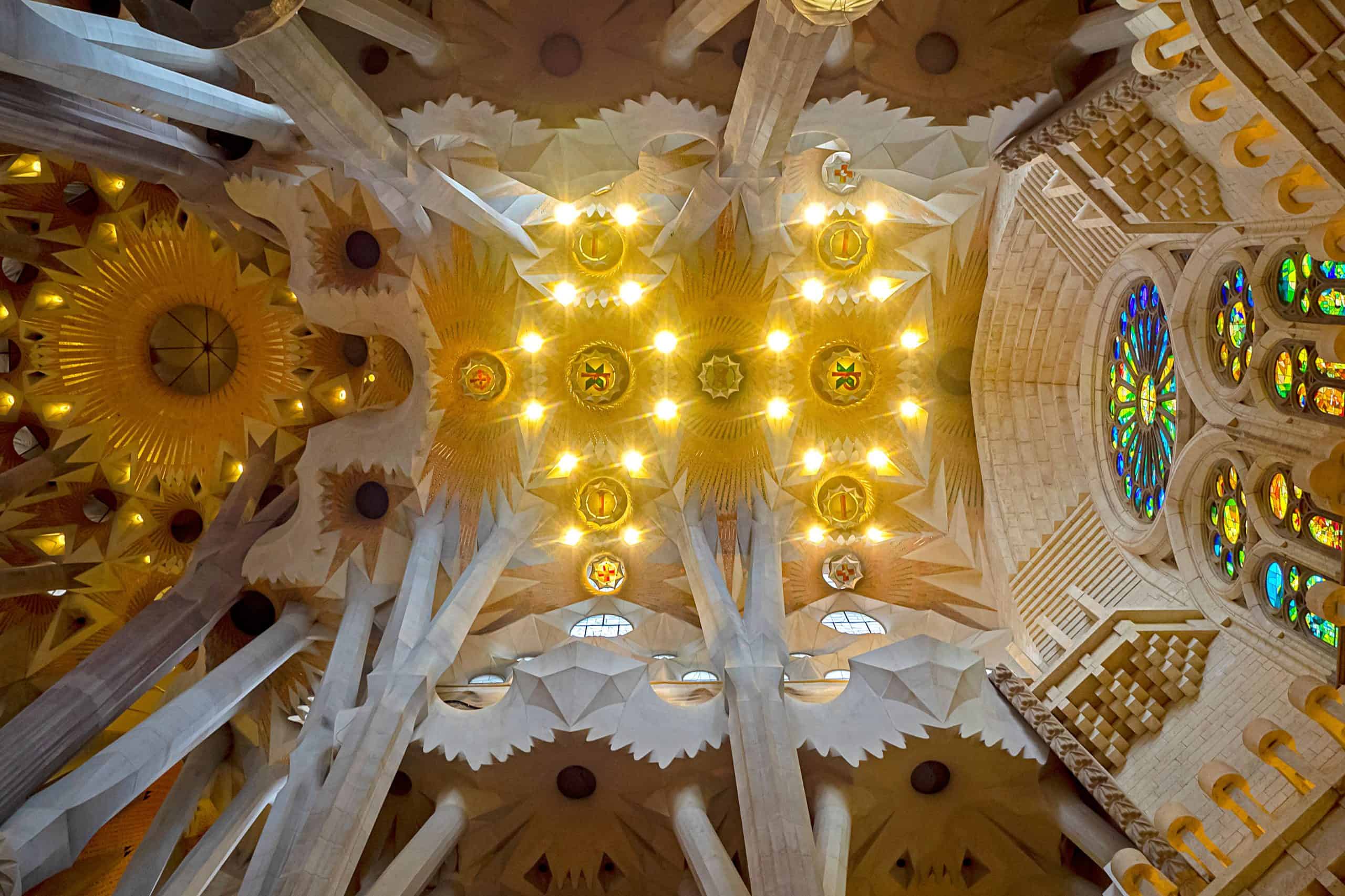 Techo y columnas del interior de la Sagrada Familia iluminados por luces cálidas y vitrales de colores.